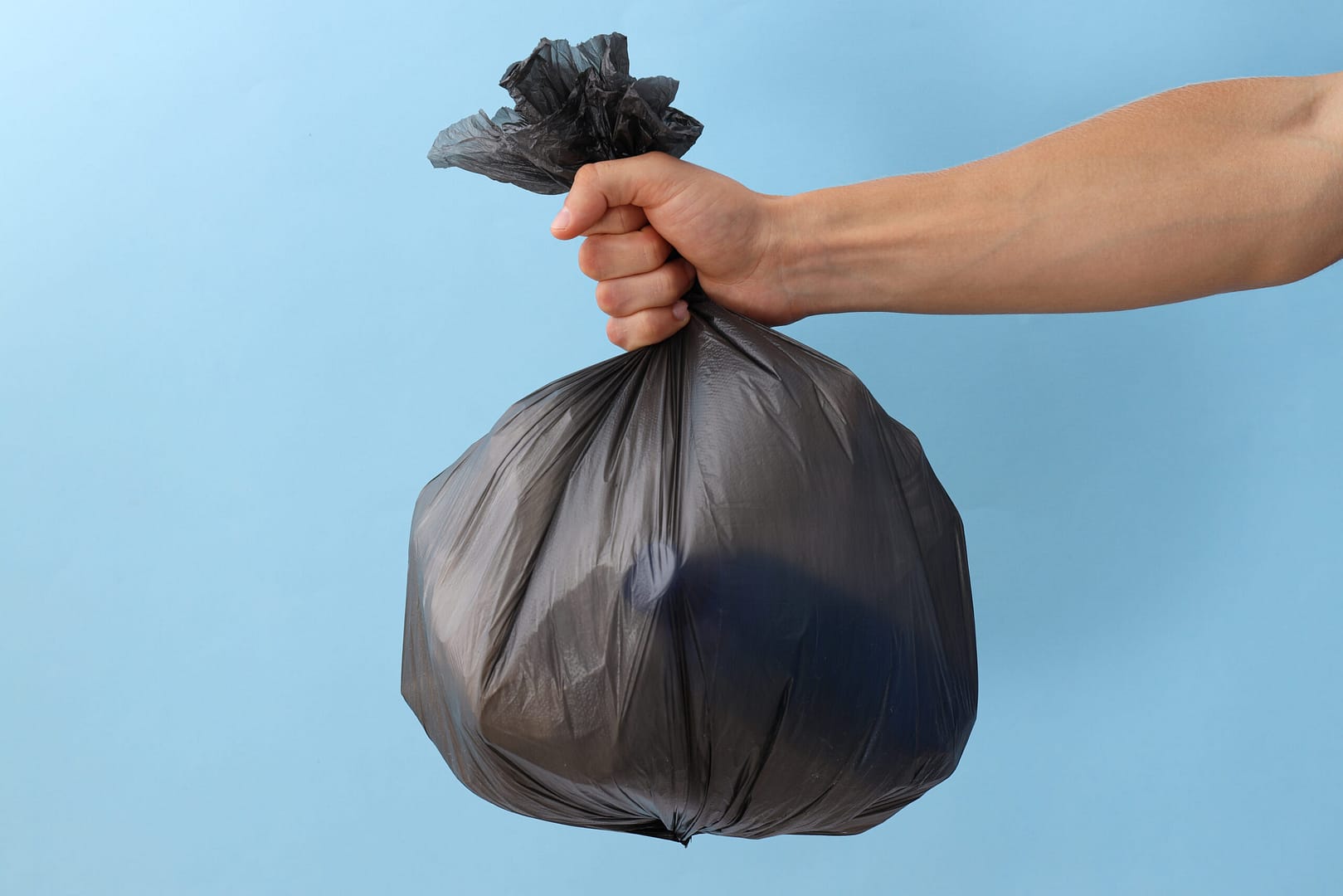 Garbage bag with rubbish in hand on blue background